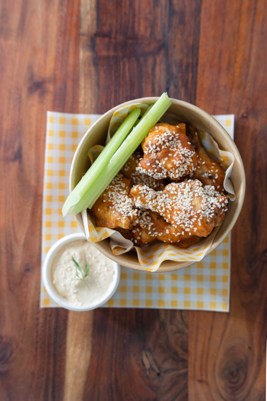 Sticky sesame chicken wings in a kraft bowl with celery and ranch
