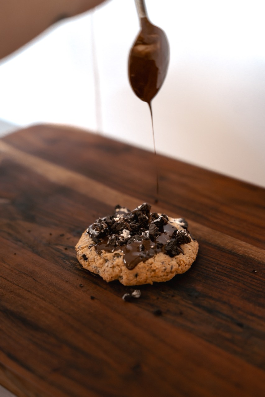 A single thick loaded cookie with chocolate being drizzled over the top